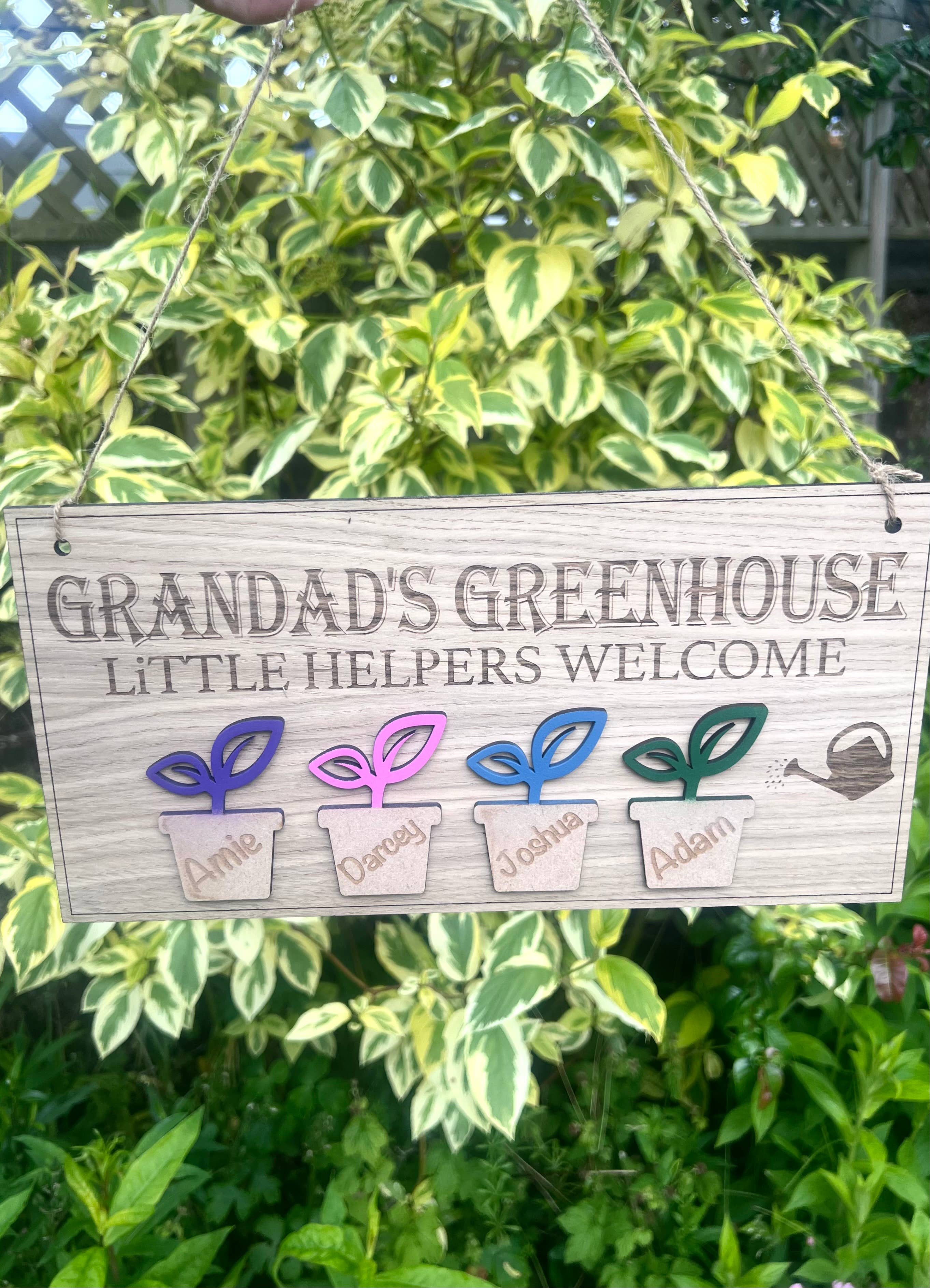 Personalised Grandadโs Greenhouse wooden sign with little helpers welcome text with 4 plant pot design hanging in a sunny garden